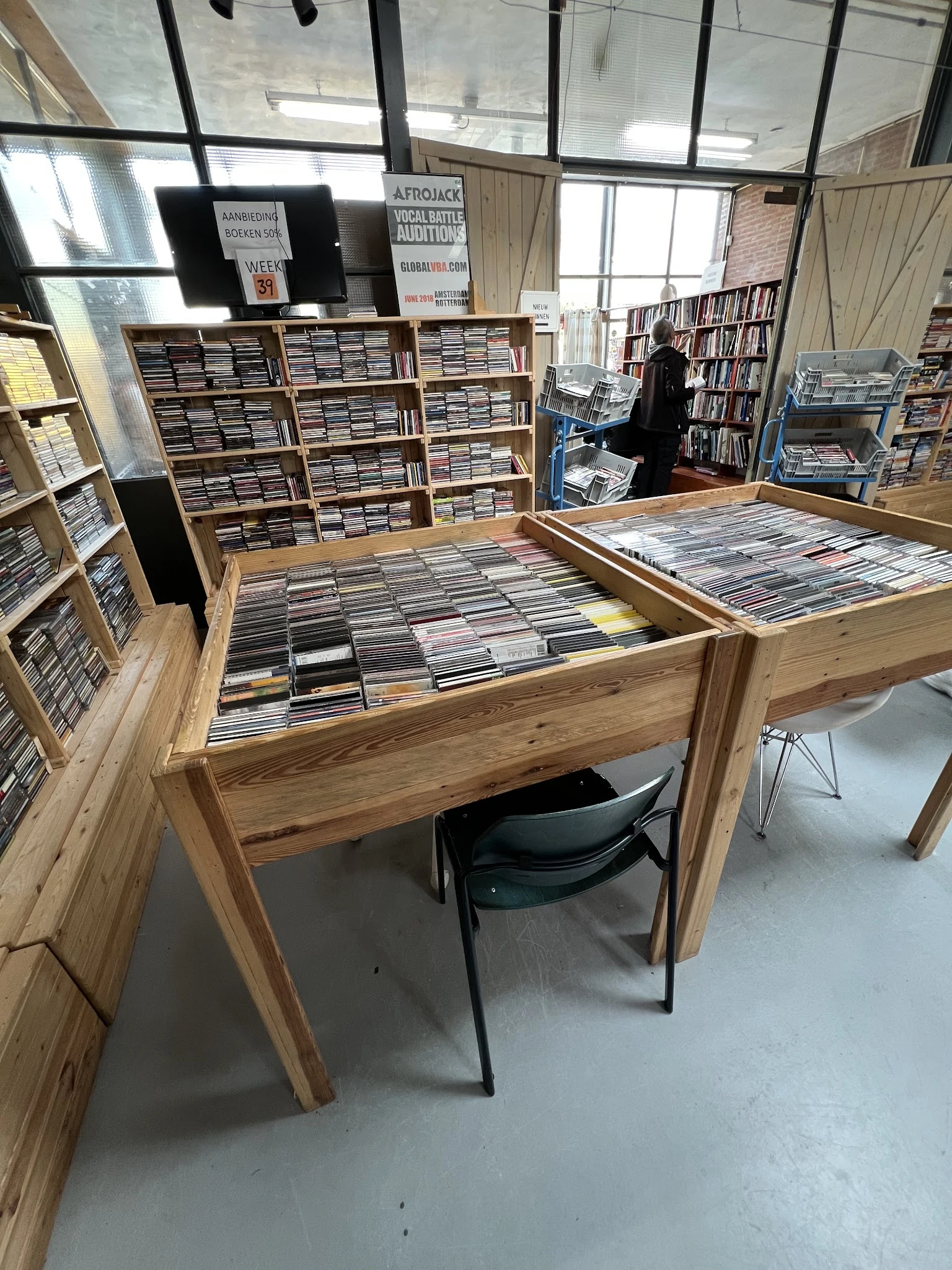 Houten displaytafels vol met uitgestalde cd's in een kringloopwinkel, met kasten op de achtergrond