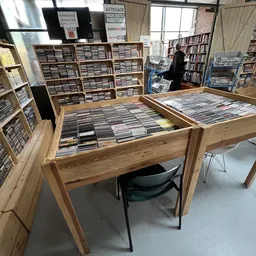 Houten displaytafels vol met uitgestalde cd's in een kringloopwinkel, met kasten op de achtergrond