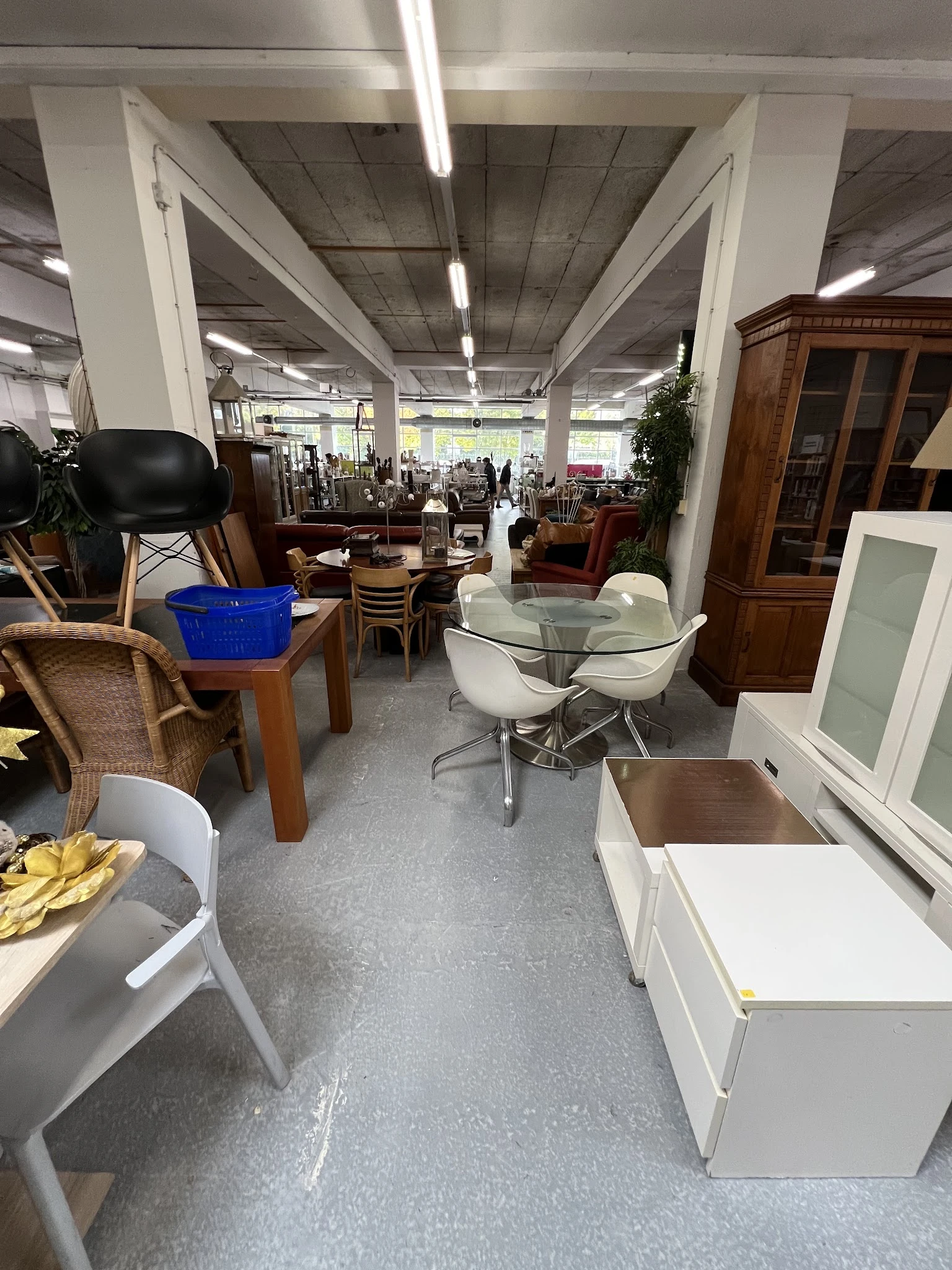 Winkelvloer met diverse meubelstukken: glazen tafel met witte stoelen, houten tafels, eetkamerstoelen, kasten en decoratie