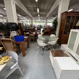 Winkelvloer met diverse meubelstukken: glazen tafel met witte stoelen, houten tafels, eetkamerstoelen, kasten en decoratie