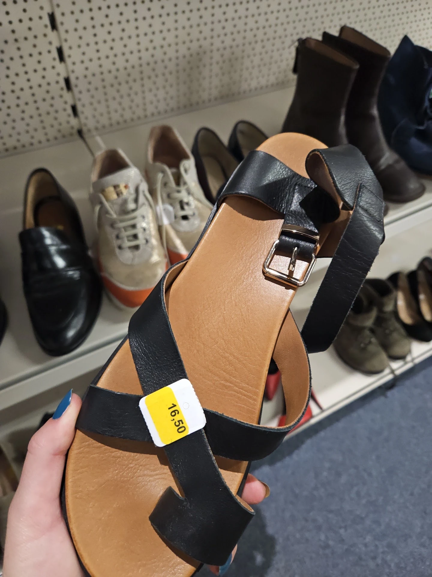 Close-up van een zwart-bruine leren sandaal met riem en gesp, met prijssticker 16,50 euro