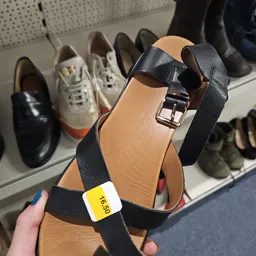 Close-up van een zwart-bruine leren sandaal met riem en gesp, met prijssticker 16,50 euro