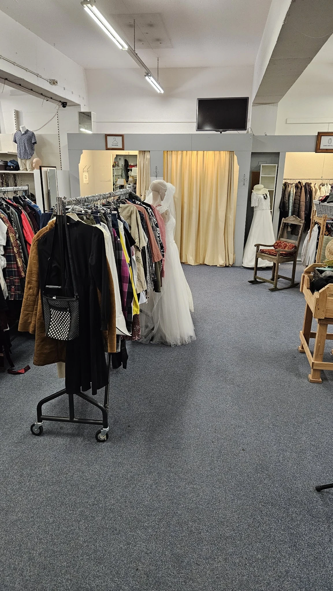 Winkelvloer met kledingrekken vol tweedehands kleding, mannequins en paskamers met gordijnen