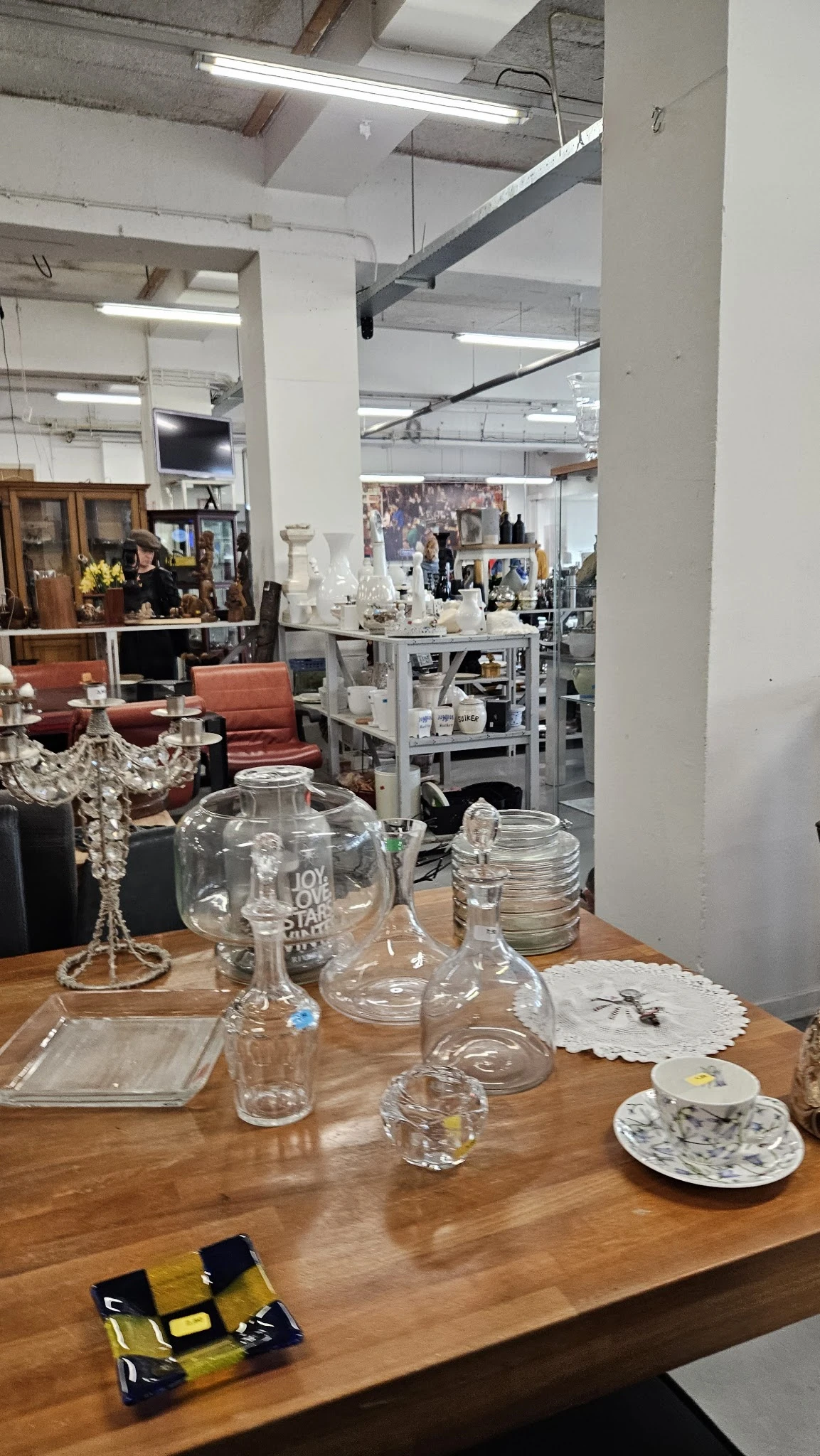 Glazen vazen en kannen op houten tafel in kringloopwinkel, op achtergrond interieur met meubels en stellingen