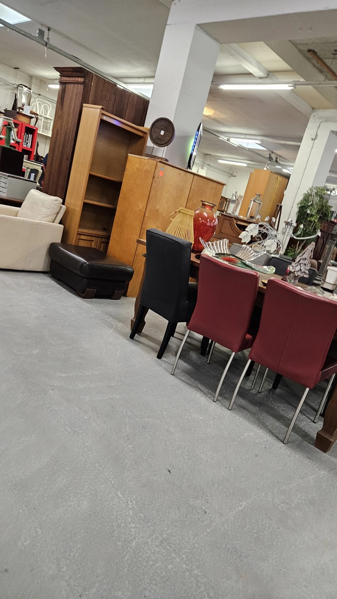 Winkelvloer met zwarte stoel, rode stoelen en houten kasten in kringloopwinkel