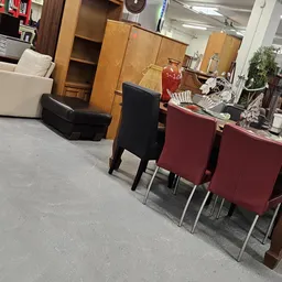 Winkelvloer met zwarte stoel, rode stoelen en houten kasten in kringloopwinkel