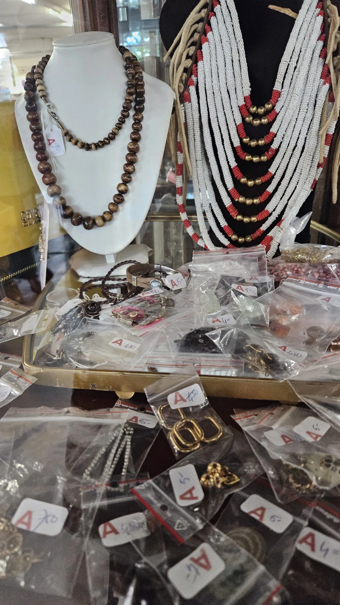 Diverse sieraden in plastic zakken en doosjes op een tafel, met kettingen op displaystandaards op de achtergrond