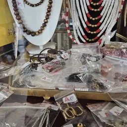 Diverse sieraden in plastic zakken en doosjes op een tafel, met kettingen op displaystandaards op de achtergrond