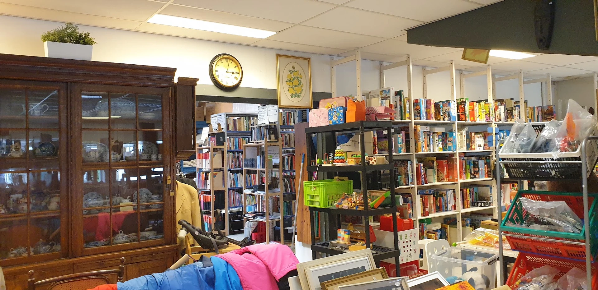 Winkelinterieur met boekenkasten, stellingen met boeken en diverse spullen, klok aan muur, vintage kast links