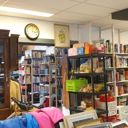 Winkelinterieur met boekenkasten, stellingen met boeken en diverse spullen, klok aan muur, vintage kast links