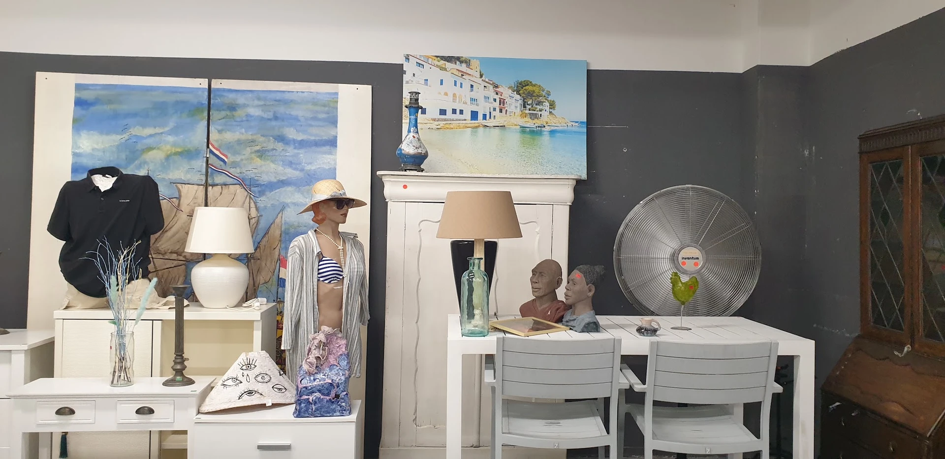 Winkelinterieur met uitgestalde meubels, een ventilator, kunstwerk aan de muur en etalagepop met kleding