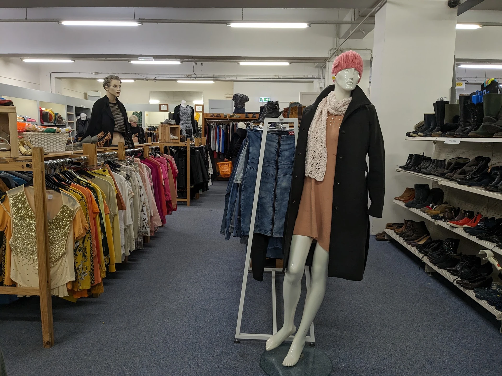 Winkelvloer met kledingrekken, etalagepop en schoenenrek in kringloopwinkel