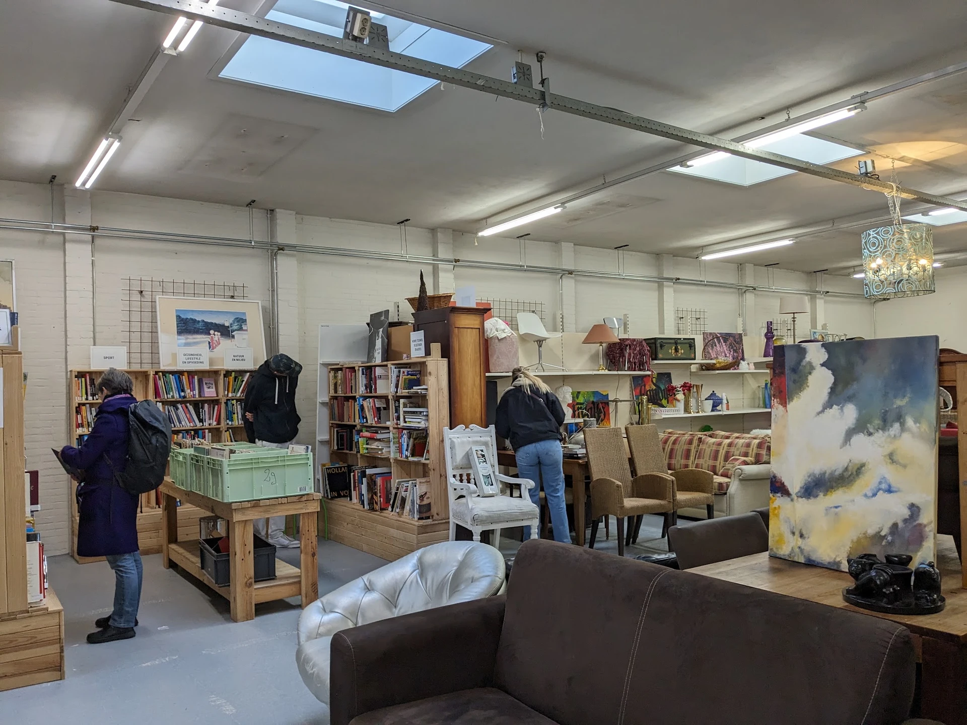Winkelvloer van kringloopwinkel met boekenkasten, zitmeubel, kunstwerk en bezoekers