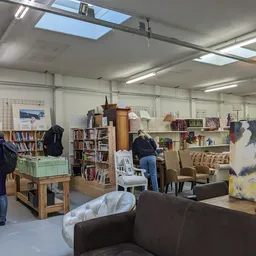 Winkelvloer van kringloopwinkel met boekenkasten, zitmeubel, kunstwerk en bezoekers