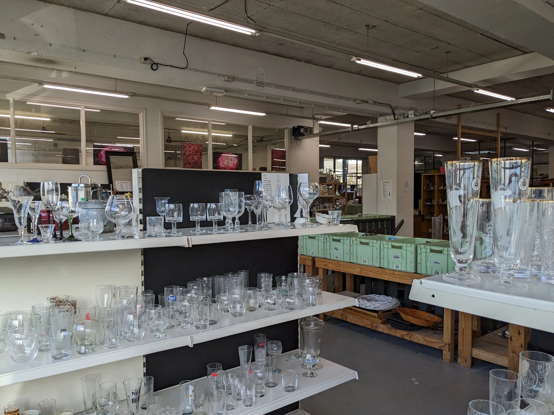 Uitgestalde glazen en drinkglazen op witte toonbanken en houten tafels in de kringloopwinkel
