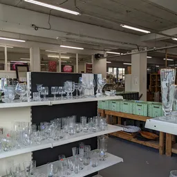 Uitgestalde glazen en drinkglazen op witte toonbanken en houten tafels in de kringloopwinkel