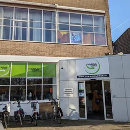 Witte gevel van kringloopwinkel met groene ramen en ingang, fietsen buiten geparkeerd