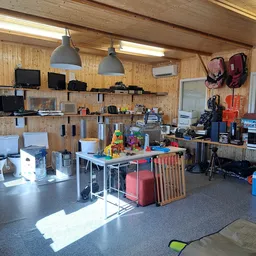 Winkelvloer met werkplekken, stellingen met elektronische apparatuur, speelgoed en diverse spullen langs de wanden