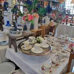 Uitgestalde vintage serviesgoed, kopjes, schotels en bloemenvazen op tafels in de winkel