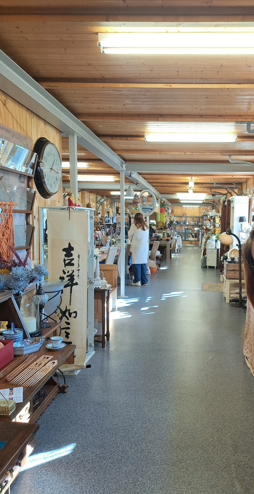 Ruim en helder winkelinterieur met houten balken, stellingen met diverse spullen, klanten aan het winkelen, natuurlijk licht 