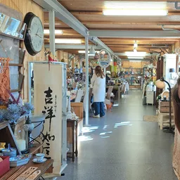 Ruim en helder winkelinterieur met houten balken, stellingen met diverse spullen, klanten aan het winkelen, natuurlijk licht 