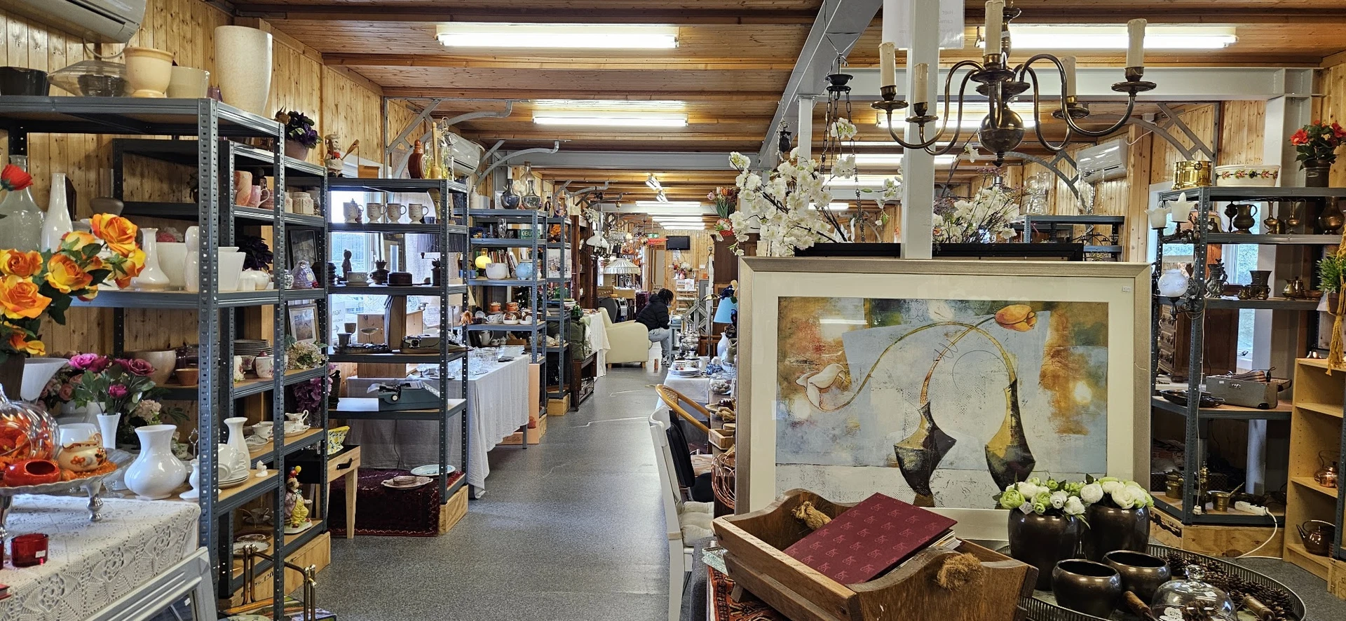 Ruim interieur van kringloopwinkel met stellingen, diverse artikelen, schilderijen, decoraties en hangende voorwerpen