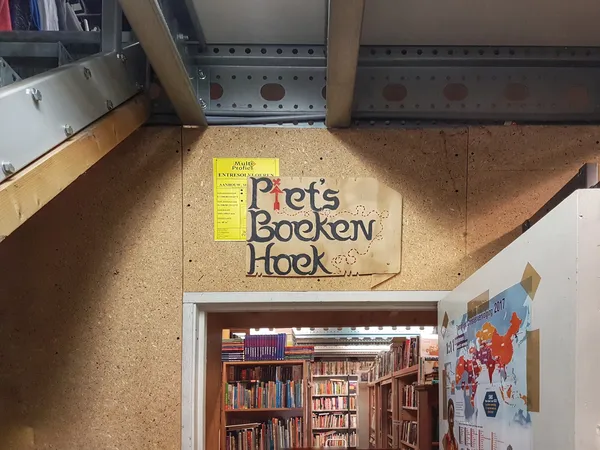 Ingang van een boekenkringloop met houten bord 'Prets Boeken Hoek' en zicht op boekenrekken binnen