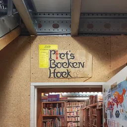 Ingang van een boekenkringloop met houten bord 'Prets Boeken Hoek' en zicht op boekenrekken binnen