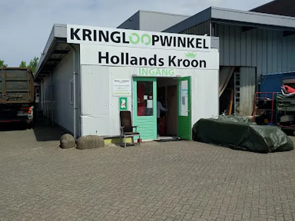 Witte gevel van kringloopwinkel met groene deur en ingang, naam duidelijk zichtbaar