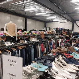 Rekken met tweedehands kleding, een etalagepop met geel shirt, en een prijsbord met 'Kleding €2,-'