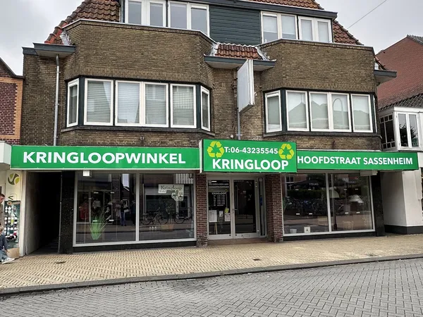 Gevel van kringloopwinkel met groene luifels, winkelnaam duidelijk zichtbaar, bakstenen voorgevel met witte raamkozijnen