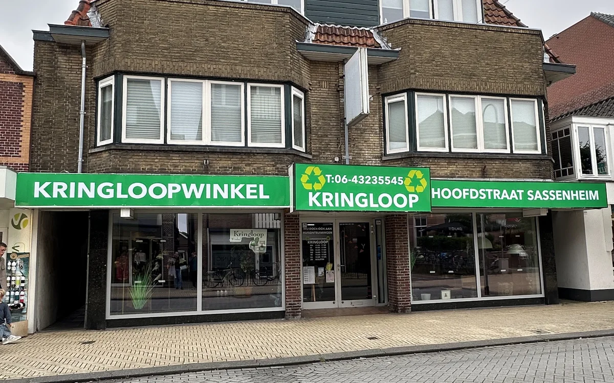 Gevel van kringloopwinkel met groene luifels, winkelnaam duidelijk zichtbaar, bakstenen voorgevel met witte raamkozijnen