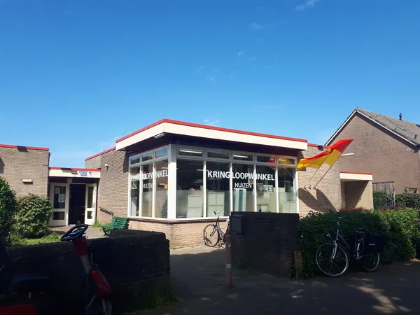 Voorgevel van kringloopwinkel met bakstenen gevel, grote ramen, rood dak en uithangbord met winkelnaam