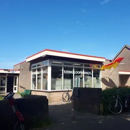 Voorgevel van kringloopwinkel met bakstenen gevel, grote ramen, rood dak en uithangbord met winkelnaam
