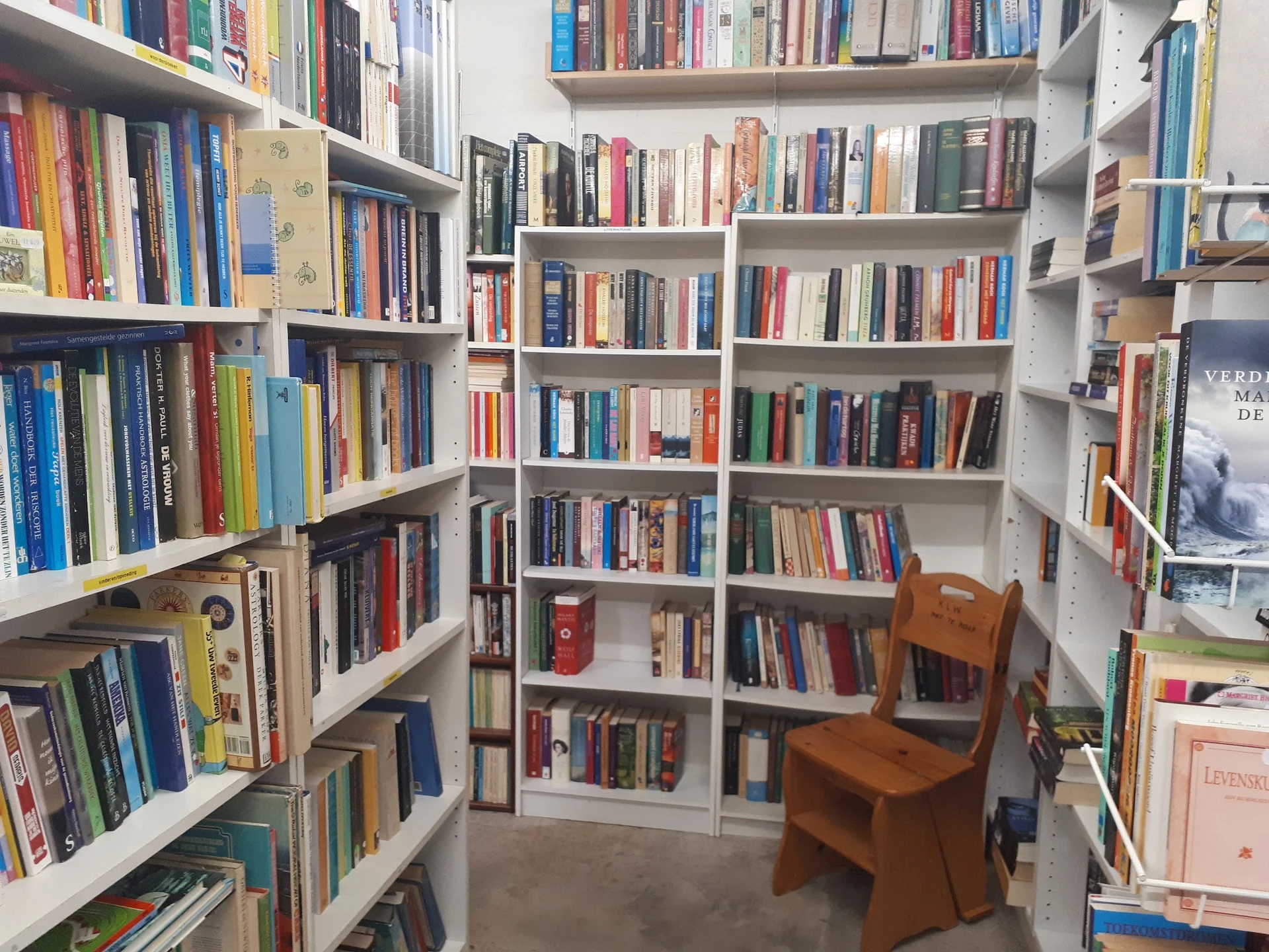 Boekenrekken langs wanden in een hoekruimte met houten stoel, kringloopwinkel met gevarieerd aanbod boeken