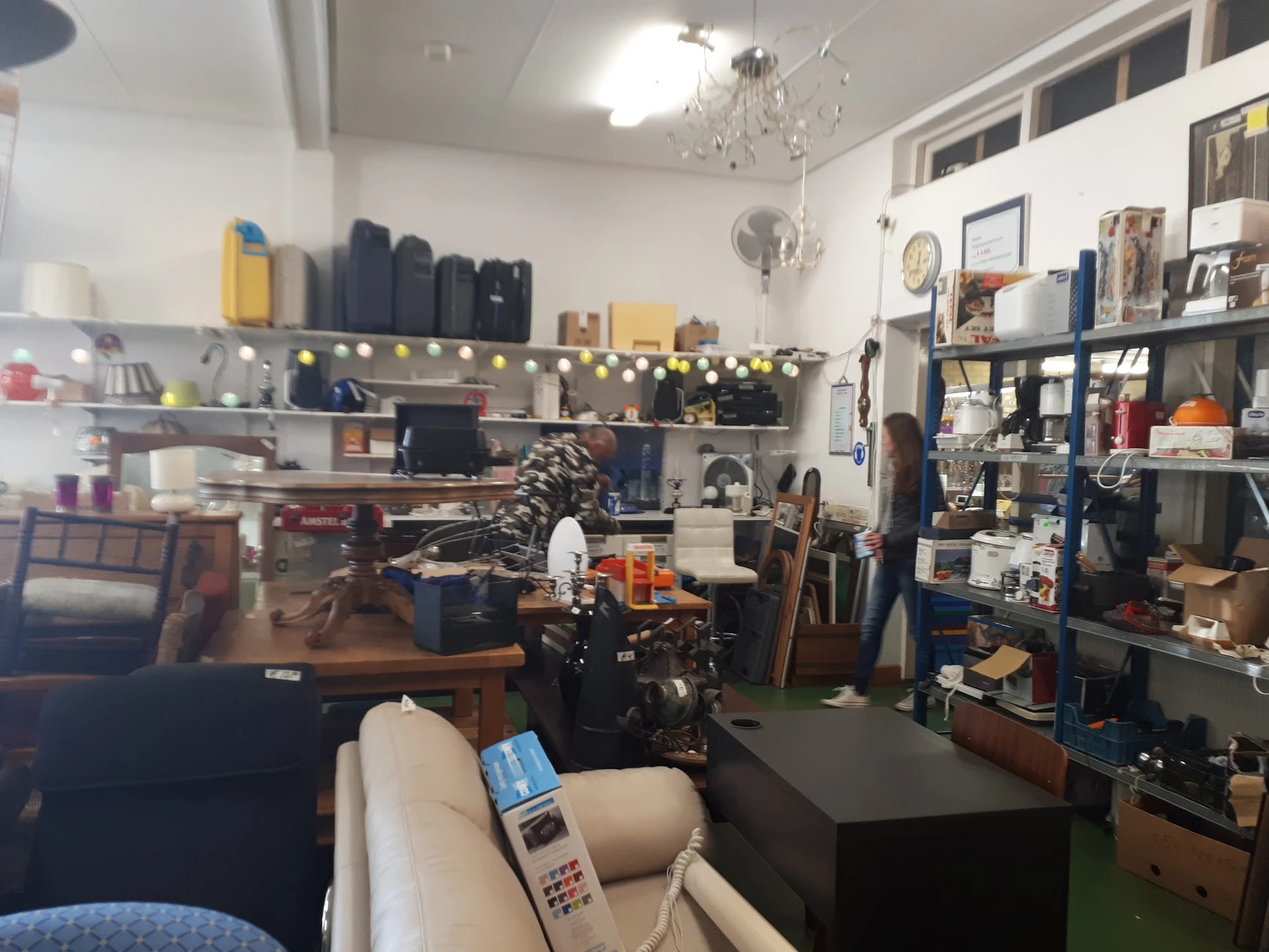 Winkelvloer met werkbanken, gereedschap, stellingen en uiteenlopende spullen in een kringloopwinkel