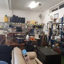 Winkelvloer met werkbanken, gereedschap, stellingen en uiteenlopende spullen in een kringloopwinkel