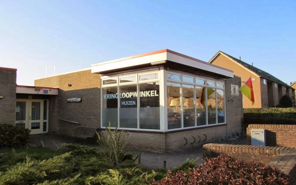 Voorgevel van kringloopwinkel met bakstenen muur, grote ramen en moderne aanbouw onder helder weer