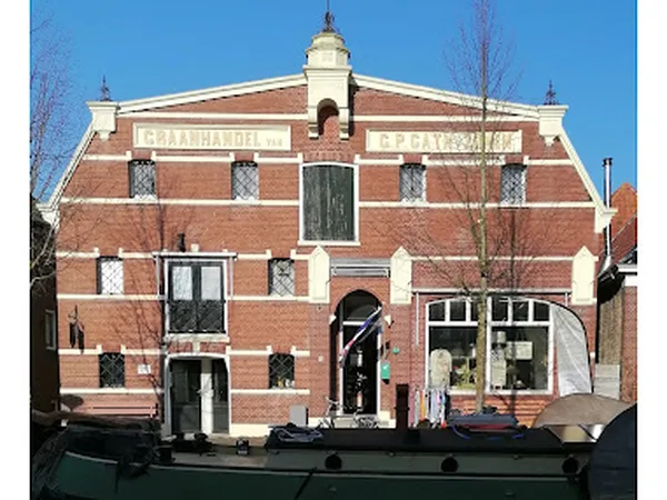 Voorgevel van rode bakstenen kringloopwinkel met witte accenten en dakkapel, gezien vanaf het water