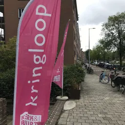 Roze vlag met 'Krimbo' logo tegen bruinsteense gevel van winkel aan straat met fietsen