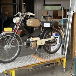 Vintage Honda brommers op gele werkplaatstafel in een werkplaats