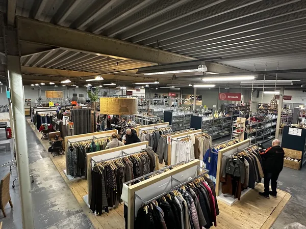 Overzicht van de winkelhal met houten display-tafels vol kleding, fluorescente verlichting en stellingen in het achtergrondge