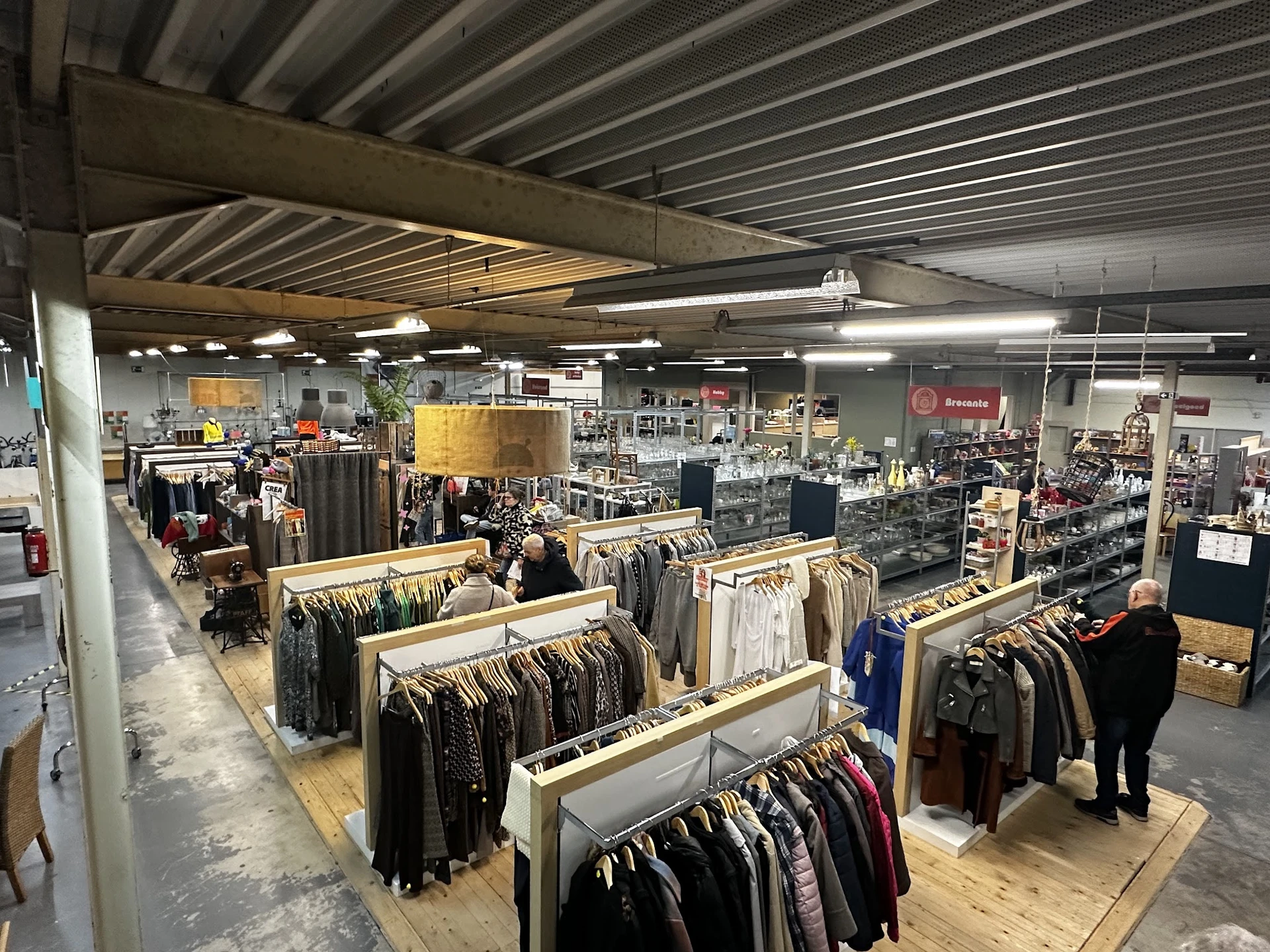 Overzicht van de winkelhal met houten display-tafels vol kleding, fluorescente verlichting en stellingen in het achtergrondge