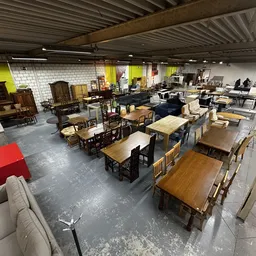 Winkelvloer met diverse meubels zoals tafels, stoelen en kasten, geel en wit geschilderde wanden