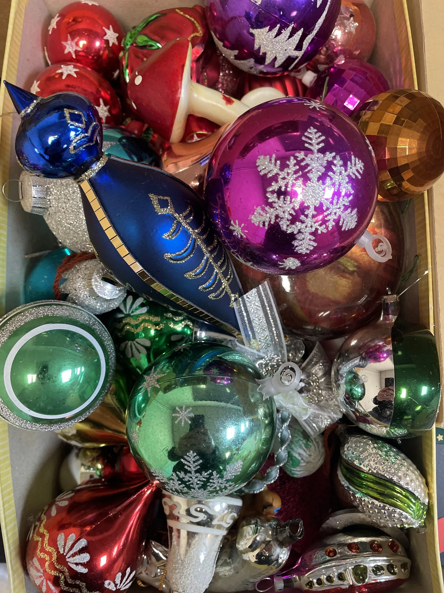 Doos met kerstballen in verschillende kleuren: blauw, paars, groen en goud met zilveren decoraties