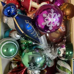 Doos met kerstballen in verschillende kleuren: blauw, paars, groen en goud met zilveren decoraties