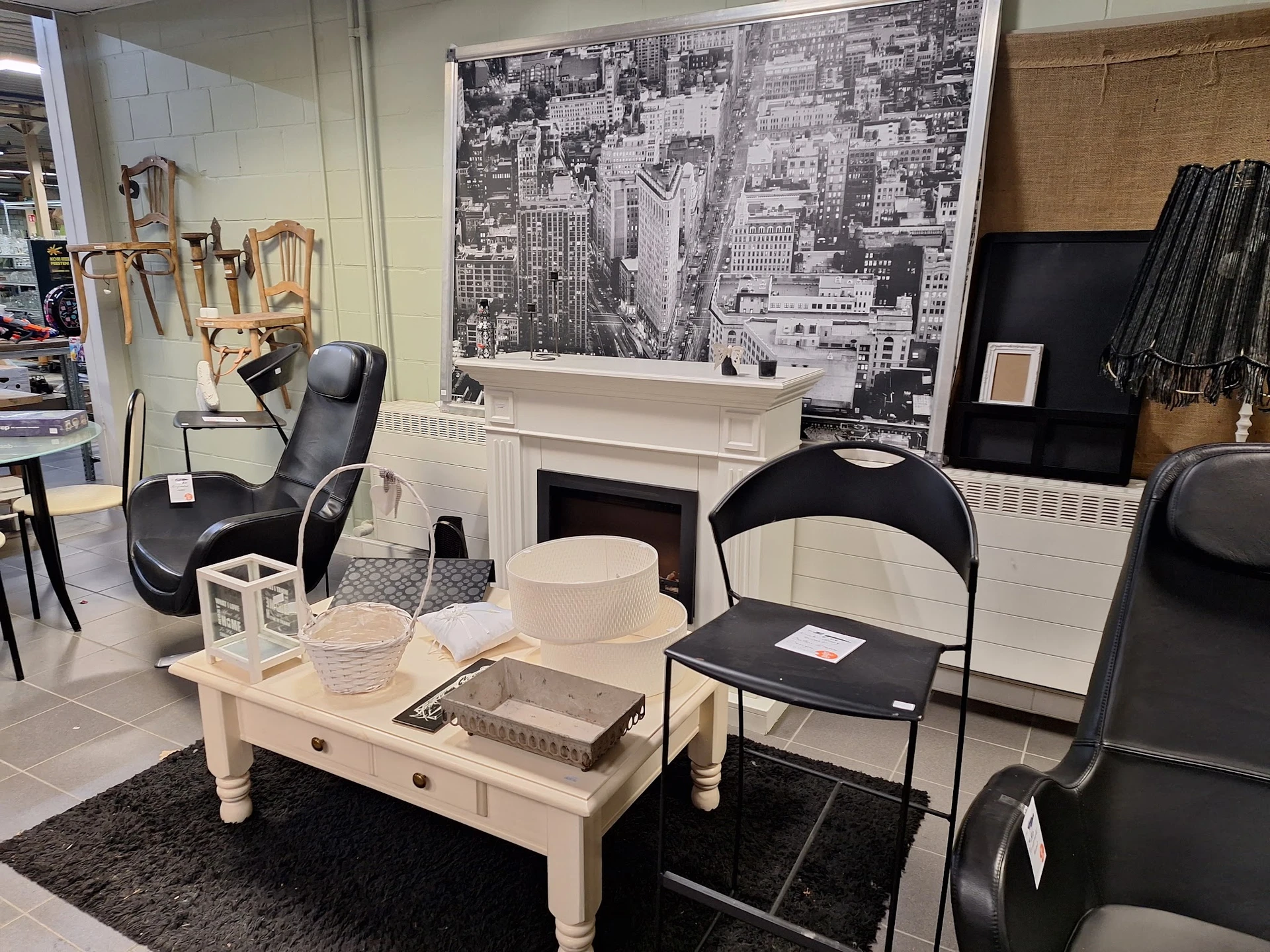 Winkelinterieur met witte salontafel, zwarte stoelen, witte boekenkast en stedenfoto aan de muur