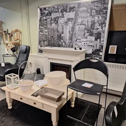 Winkelinterieur met witte salontafel, zwarte stoelen, witte boekenkast en stedenfoto aan de muur