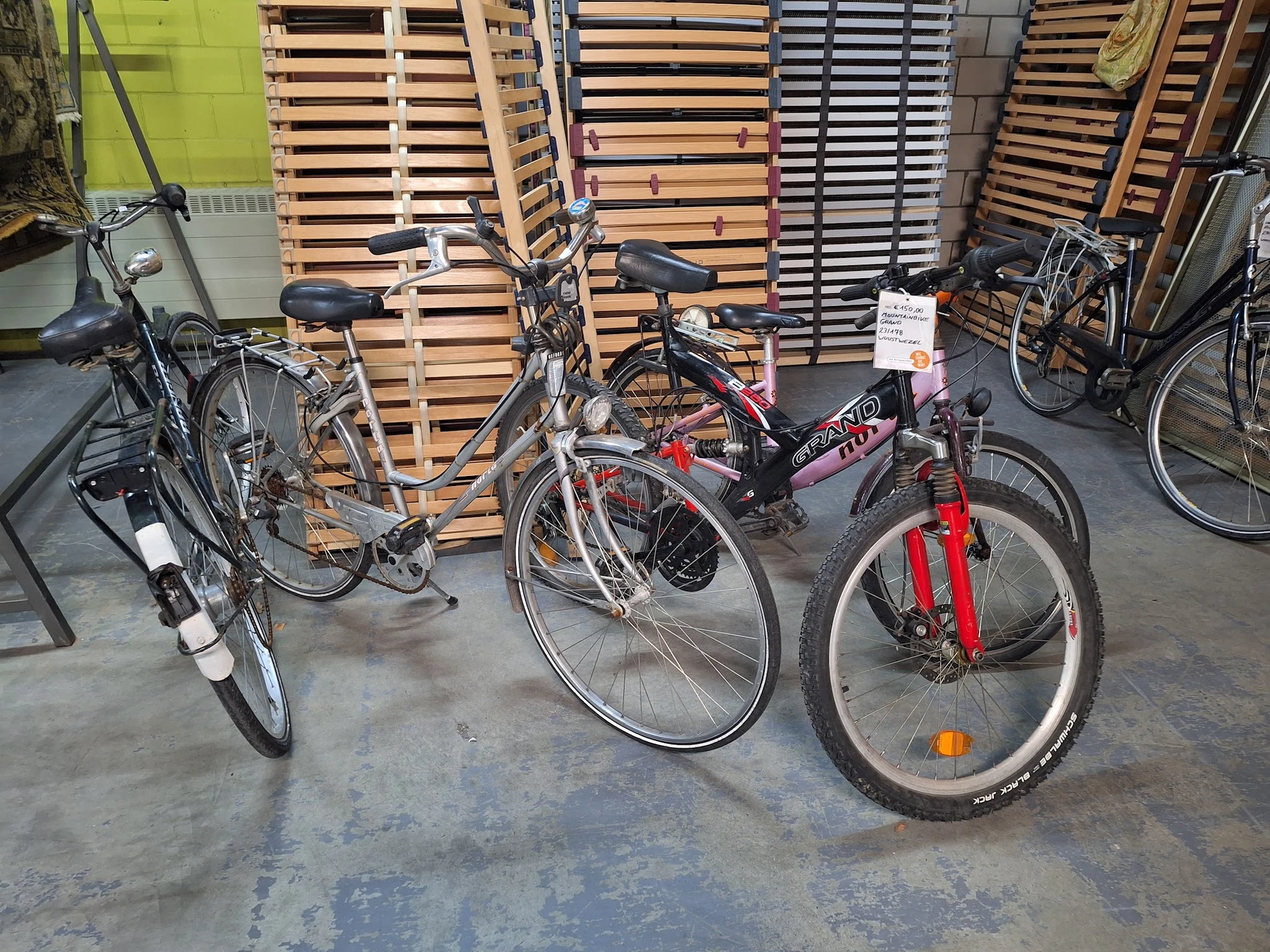 Drie tweedehandsfietsen uitgestald in de winkel, naast houten pallets