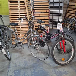 Drie tweedehandsfietsen uitgestald in de winkel, naast houten pallets